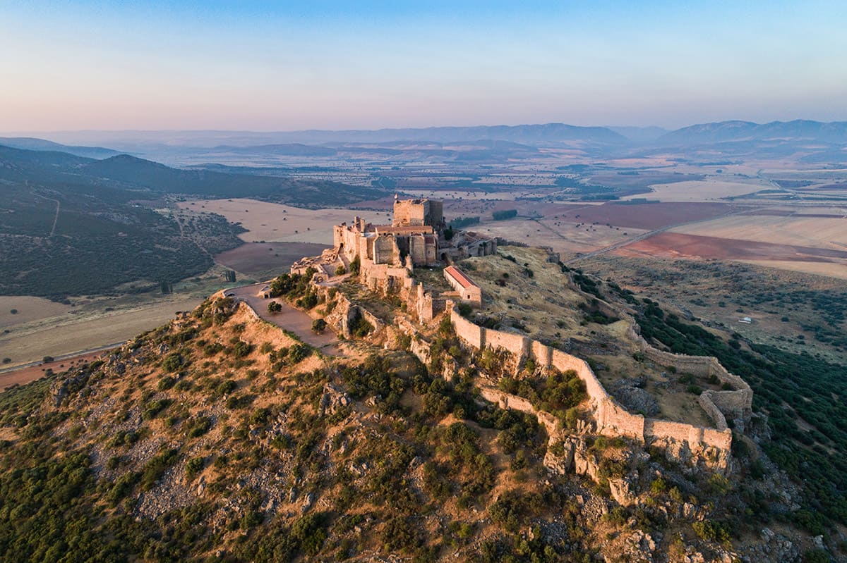 Castillo medieval en lo alto de un cerro al amanecer, sobre la llanura de Ciudad Real