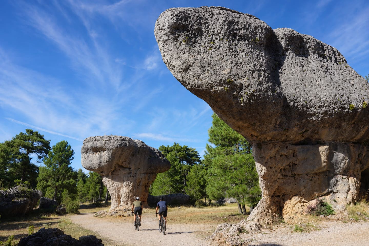 Dos ciclistas de gravel por un camino de tierra entre grandes rocas calizas con forma de seta y pinares
