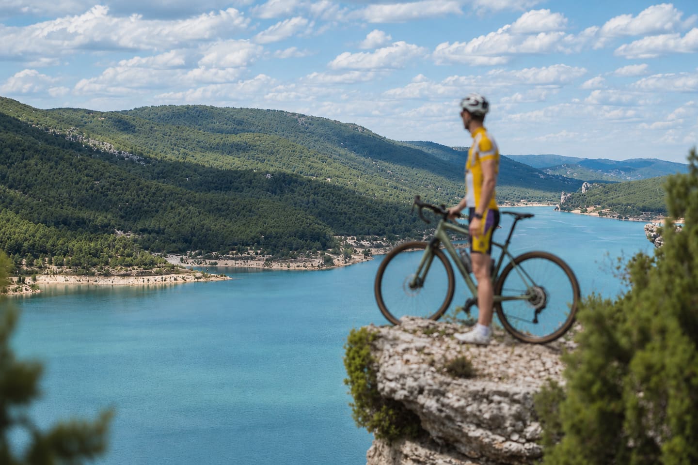 Ciclista con su bicicleta gravel sobre un saliente de roca, frente a un embalse turquesa entre pinares
